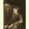 Amelia Earhart seated, wearing a leather jacket and scarf, gazing slightly to the side.
