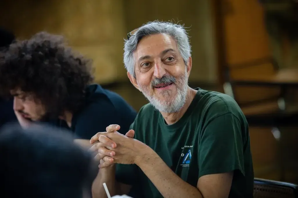 Avi Wigderson, in a green shirt, sits at a table with his hands folded