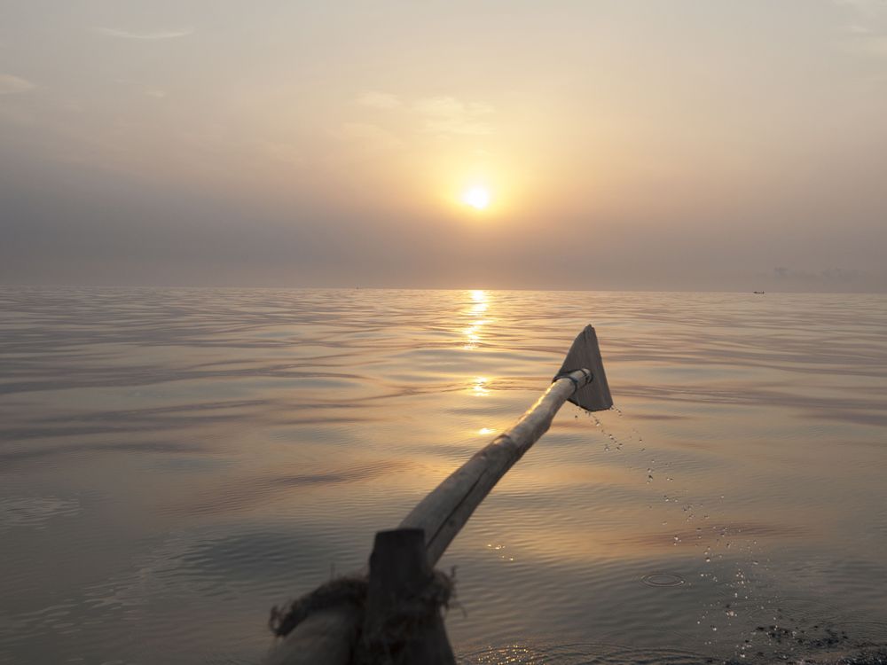 A view of an oar raised parallel to the water as the sun slowly sets