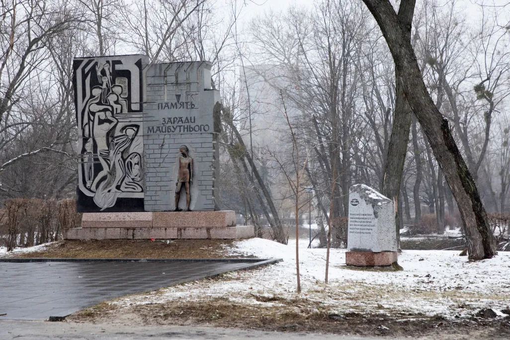 snowy view of a monument with a bronze statue of a man standing in front of a wall with Ukrainian writing