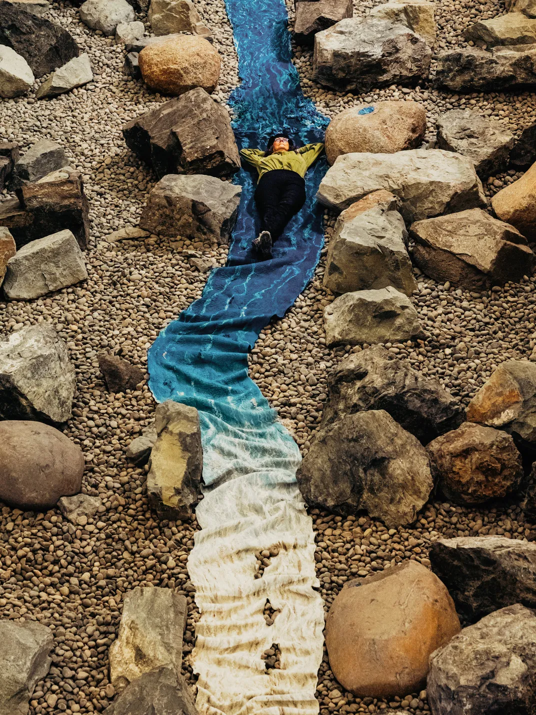 a woman lays on a fabric installation mimicking a rivers flow surrounded by boulders and rocks