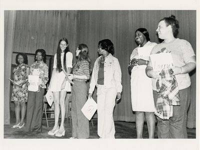 Candid photo of seven women holding papers standing in a line on stage.