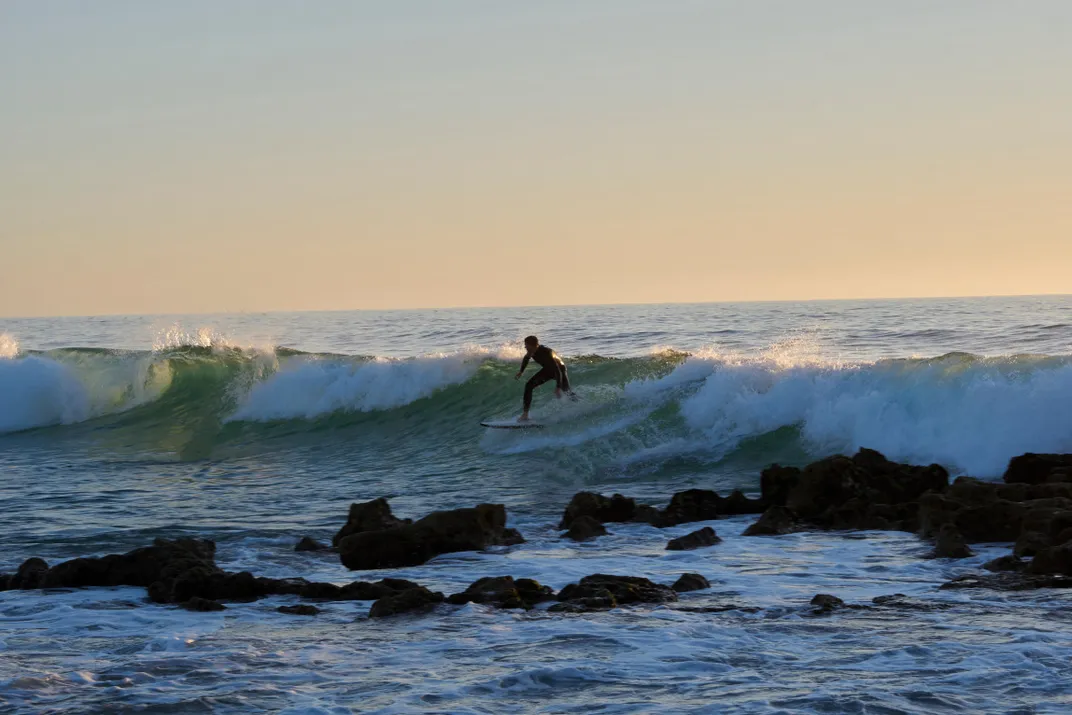a surfer on a wave behind some rocks