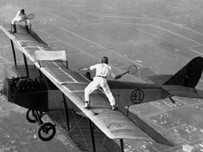 Gladys Roy and Ivan Unger play tennis on the wing of a biplane in flight, 1925.