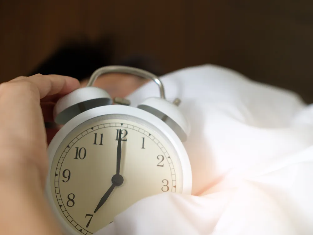 Alarm clock on a bed sheet with a person's hand