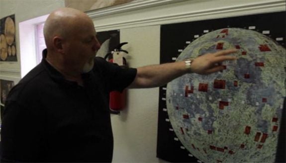Dennis Hope stands next to a map of the Moon, showing (in red) all the plots of land he’s sold.