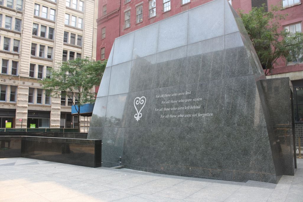 A monument in a city square, consisting of a large slab of dark stone with the words 'For all those who were lost, for all those who were stolen, for all those who were left behind, for all those who were not forgotten'