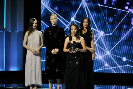 Winner Hillary Andales accepts her “science Oscar” from  actress Lily Collins (left) and philanthropist Julia Milner (next to Collins), as her stage escort waits.
