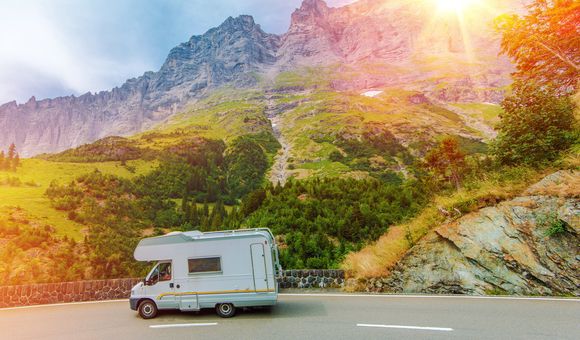 Sun shines brightly on a mountain landscape scene depicting a road with an RV