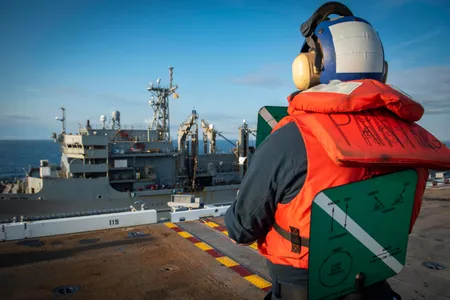 Seaman Matthew Kortie of the USS George H.W. Bush Deck Department stands watch as signalman during a weekly replenishment at sea. An aircraft carrier’s Supply Department may do more than a dozen jobs, including paying and feeding sailors, managing repair parts, equipping its medical and dental staffs, and running barbershops, convenience stores, and its own version of a Starbucks.   
