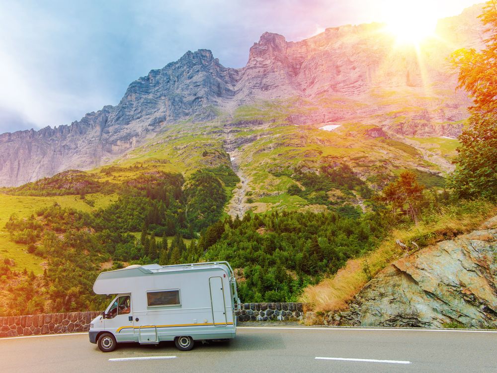 Sun shines brightly on a mountain landscape scene depicting a road with an RV