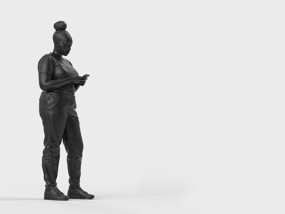 A bronze statue of a black woman surrounded by a plain white background. The woman is standing casually and looking down at her mobile phone, which she holds with both hands.