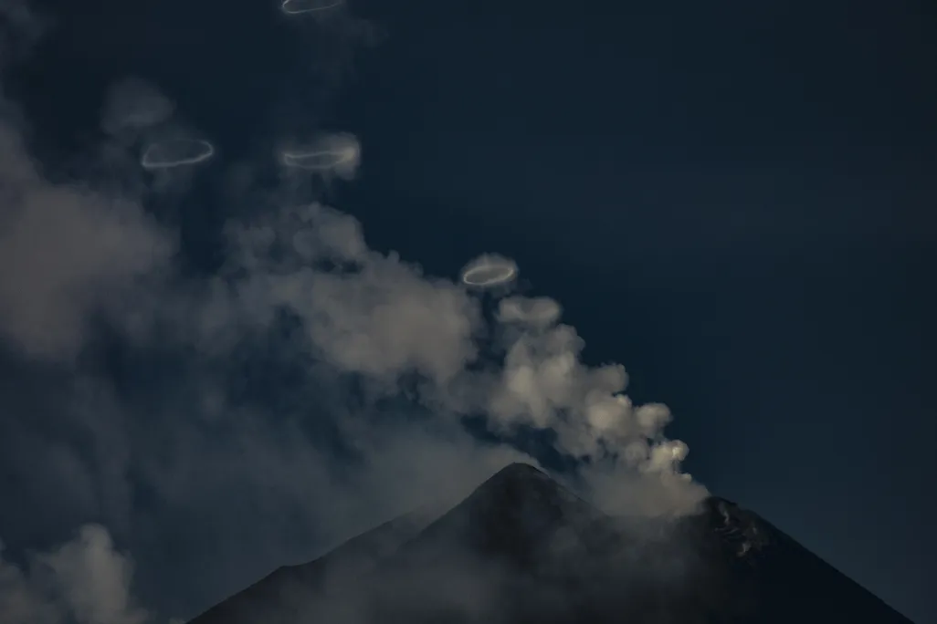 A volcano with wisps of clouds and rings floating above