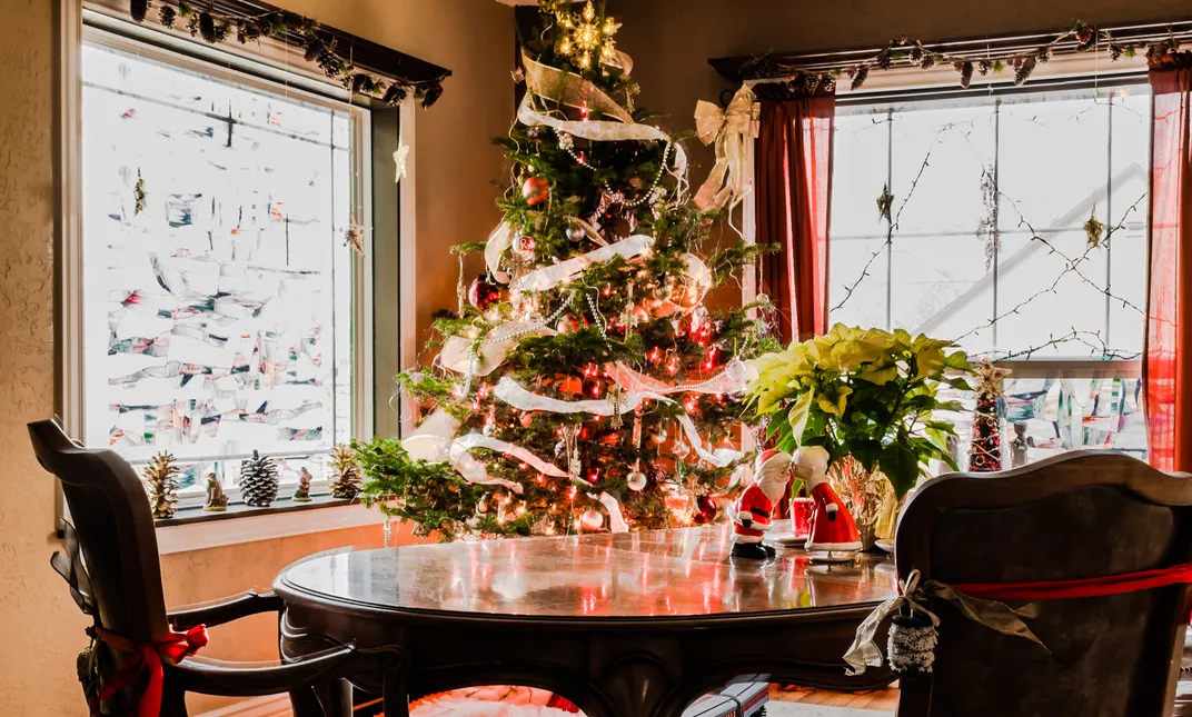 A miniature statue of Santa Claus and his wife kissing on a table in front of a Christmas tree