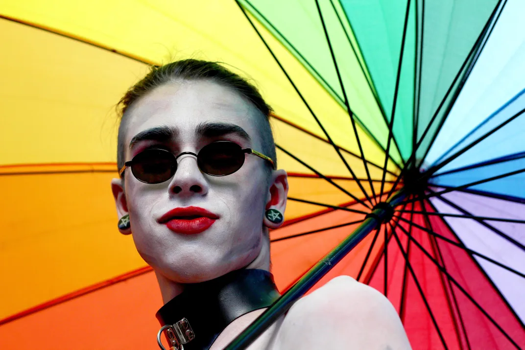 a person in makeup under a rainbow colored umprella
