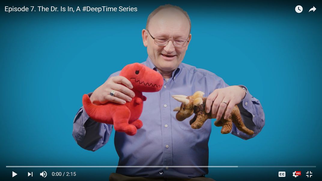 Person holding two stuffed dinosaur toys.