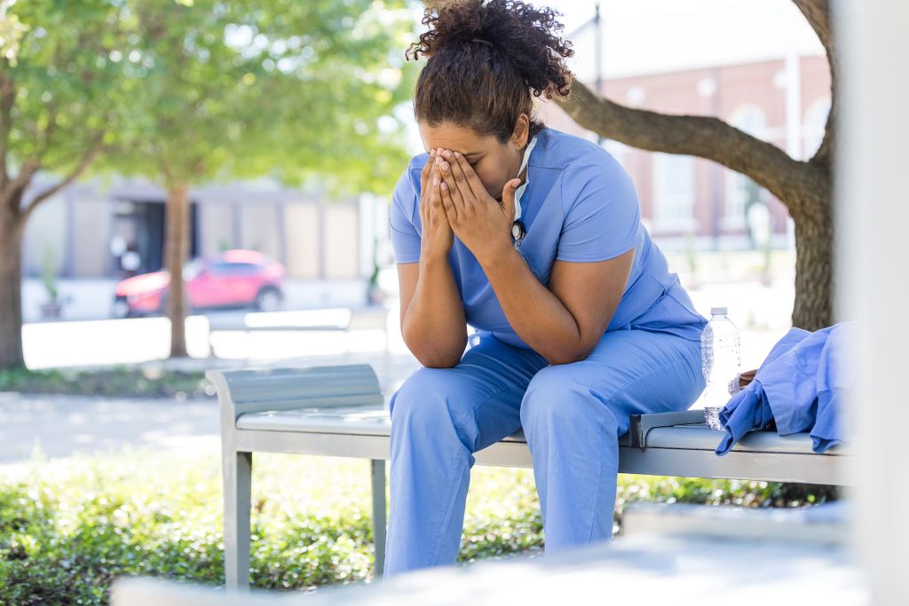A healthcare worker sits outside with her head in her hands