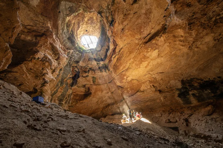 OPENER - A shaft of golden light from the cave’s mouth provides warmth as the expedition’s scientists enjoy lunch 80 feet below the opening of Natural Trap Cave.