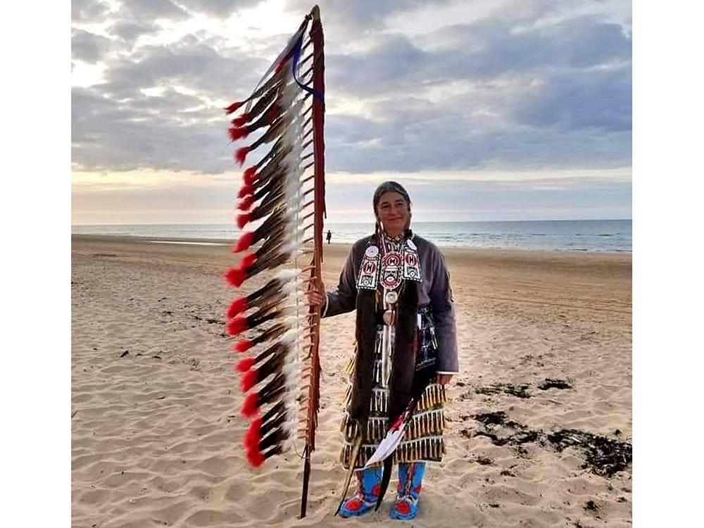 Command Sergeant Major Julia Kelly (U.S. Army retired), one of 80 Native American delegates to the 75th anniversary observance of D-Day, stands on Omaha Beach. Kelly holds an eagle feather staff, an American Indian symbol of respect, honor, and patriotism. (Courtesy of Julia Kelly)