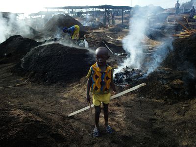 A child stands in the Côte d’Ivoire charcoal yard where his mother works.