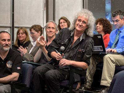 Astrophysicist Dr. Brian May is recognized during a July 17, 2015 New Horizons science briefing at NASA Headquarters, Washington, D.C. May spent a long birthday weekend with the science team, attending two morning science plenaries, a meeting with the Student Dust Counter group, and working on stereo images of Pluto with the Geology, Geophysics and Imaging (GGI) team.