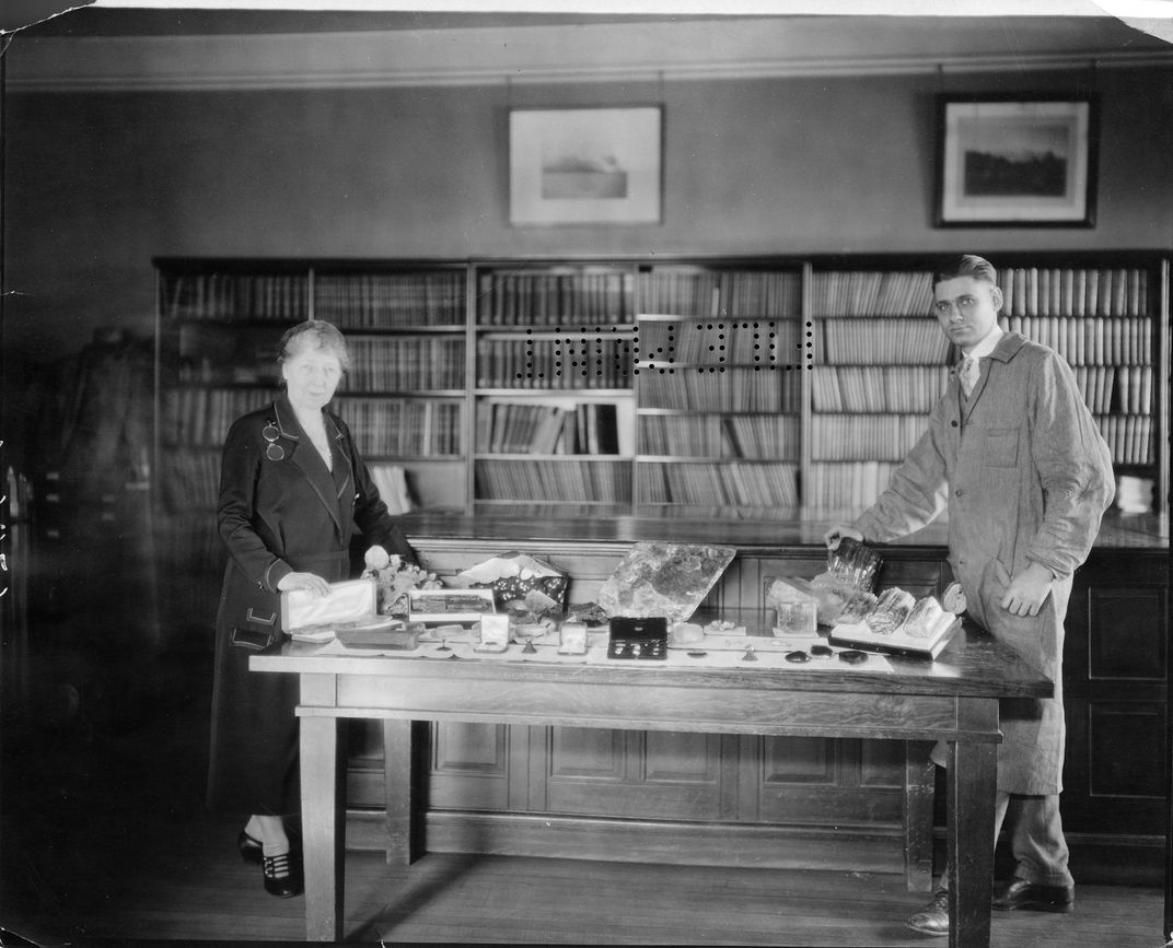 Black and white photo of Margaret Moodey and William Foshag standing in a museum space next to a table full of minerals of varying sizes