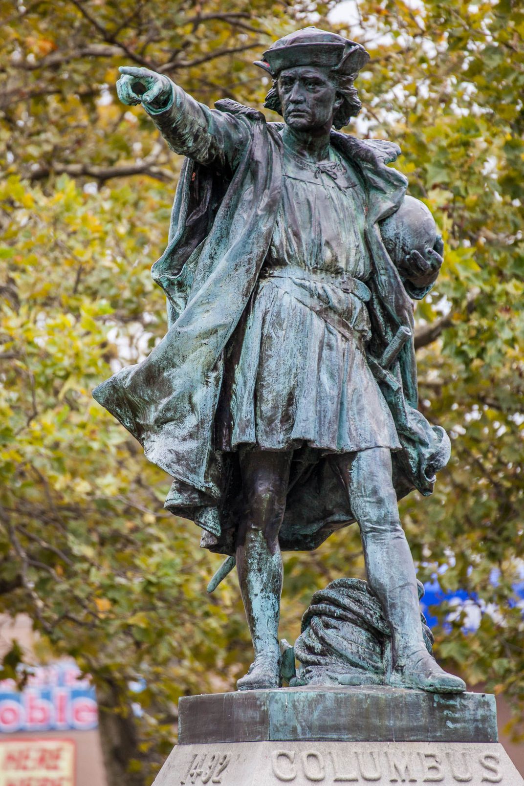 A silvery blue statue of Columbus, holding a globe and pointing with his finger in an authoritative stance