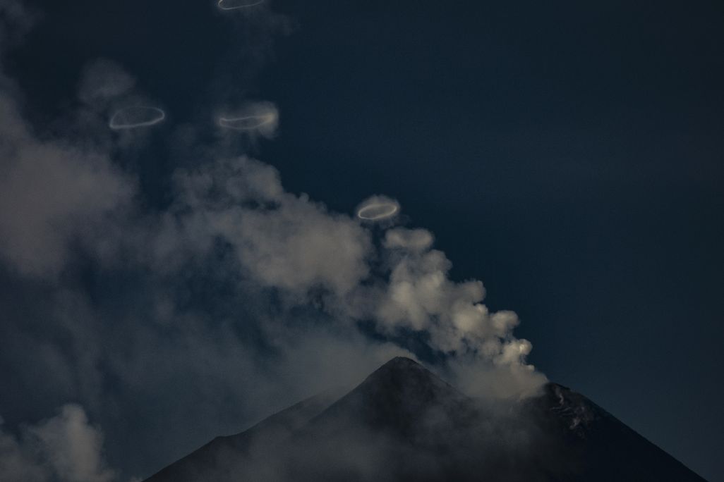 A volcano with wisps of clouds and rings floating above