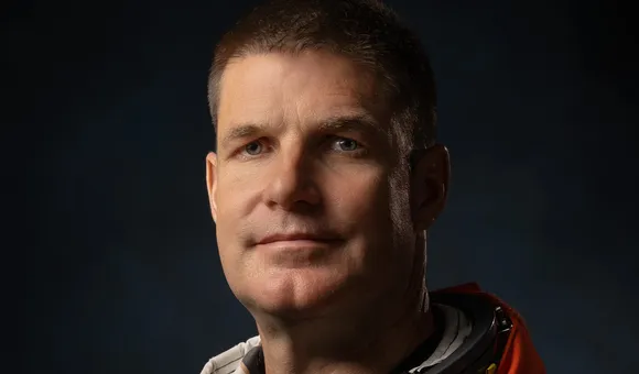 Dramatically-shot portrait of a white male astronaut in an orange spacesuit.