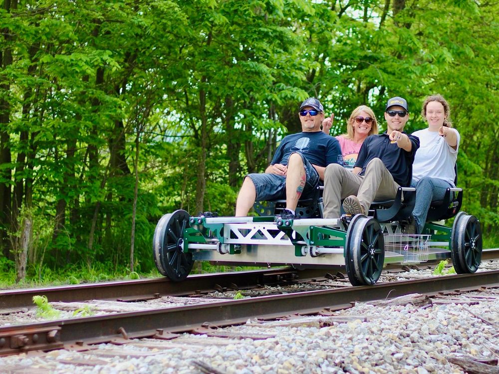 Group of four people riding a railbike while pointing at the camera and smiling