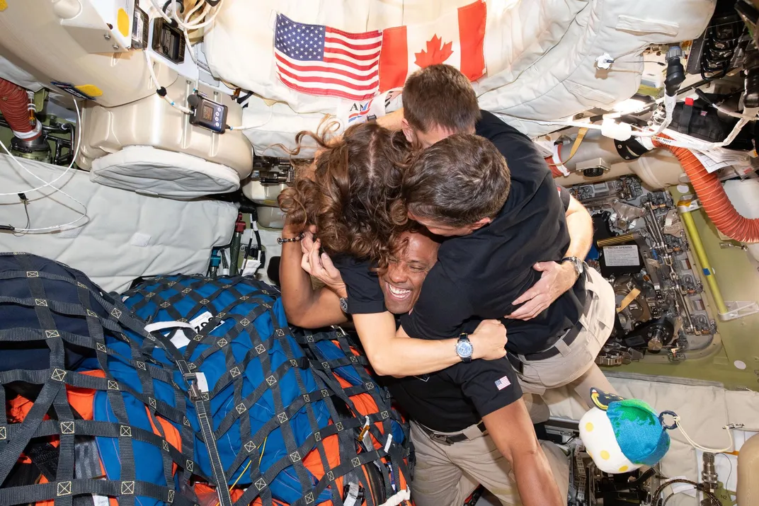 within the Orion capsule, the four astronauts embrace in a hug, Victor Glover's smiling face visible through the huddle