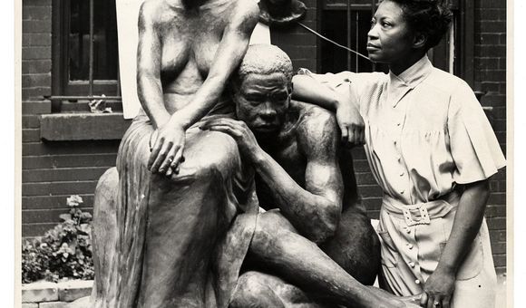 A black and white photograph of artist Augusta Savage standing next to her sculpture