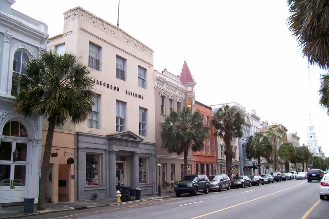 A downtown street lined with palm trees and storefronts painted in pastel colors.