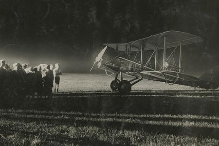 A crowd stands near a mailplane equipped with lights on the nose and wingtips for night flying, sometime in the mid-1920s.
