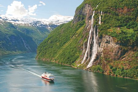 A Hurtigruten cruise sails through Geirangerfjord, Norway, renowned for its cascading waterfalls and UNESCO World Heritage sites.