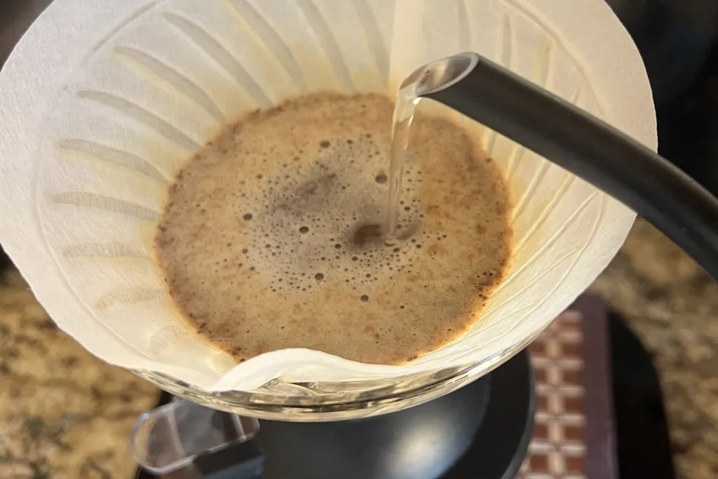 coffee grounds and water in a coffee filter as a goose-neck kettle pours a flow of water in