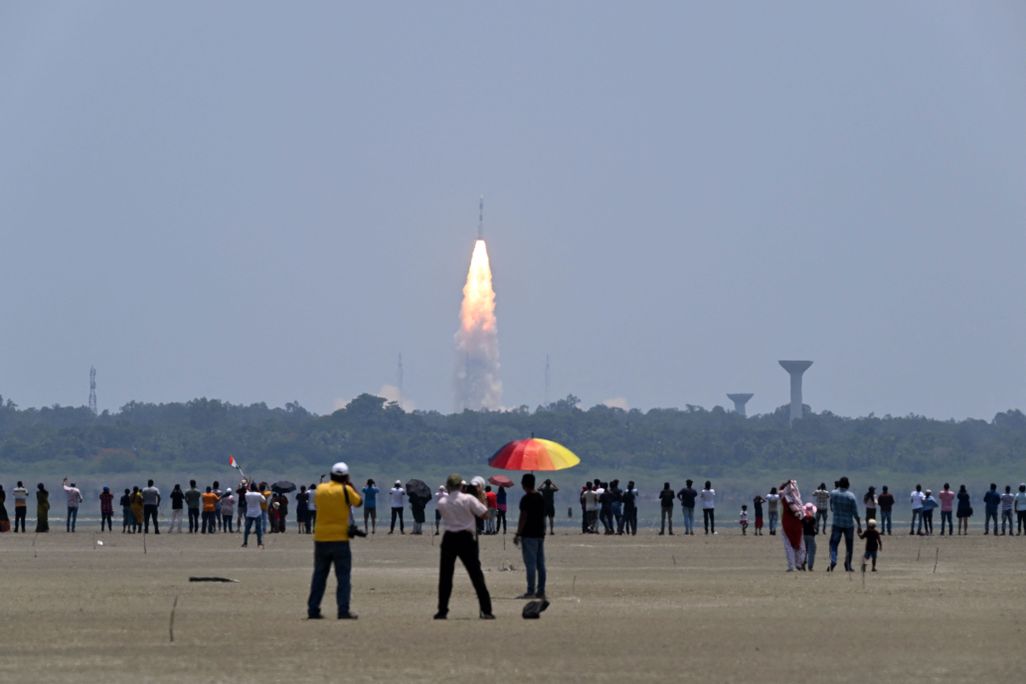 People stand and watch as a rocket takes off in the background