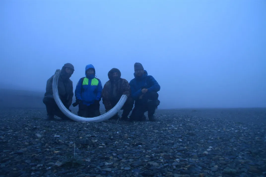 Team of people holding up a mammoth tusk in murky blue light