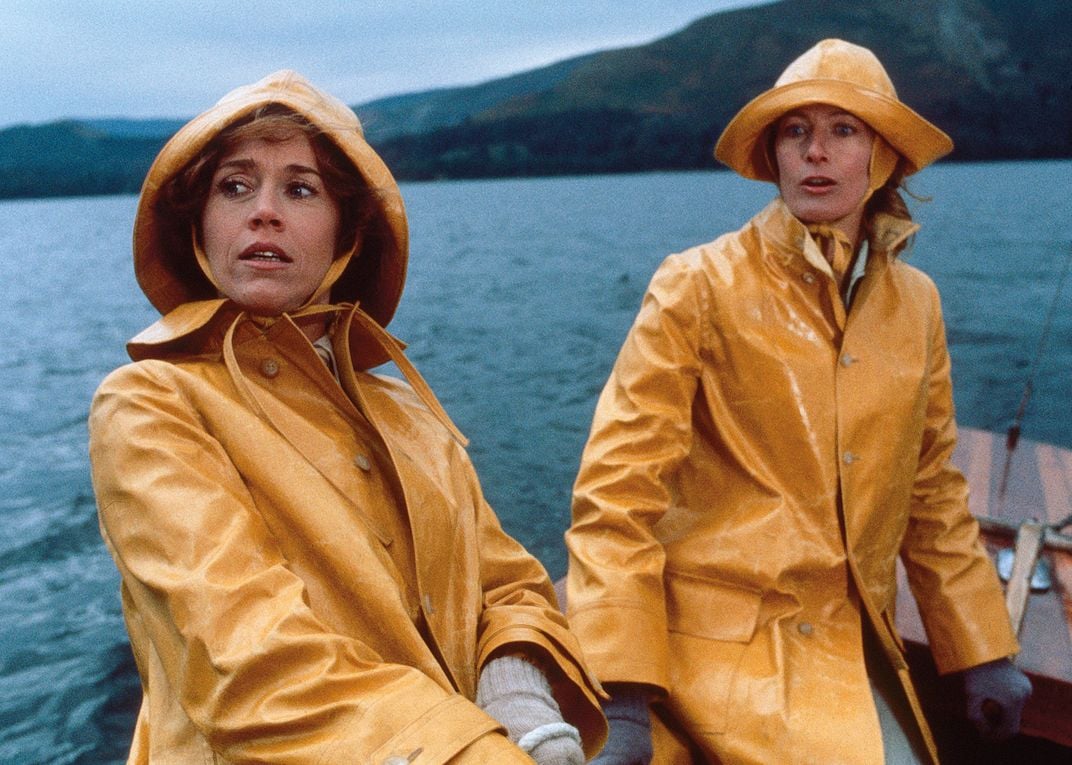 two women in yellow rain jacket and cap cross a lake on a small boat