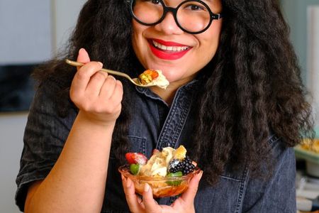 Image shows a smiling woman eating a bowl of fruit.