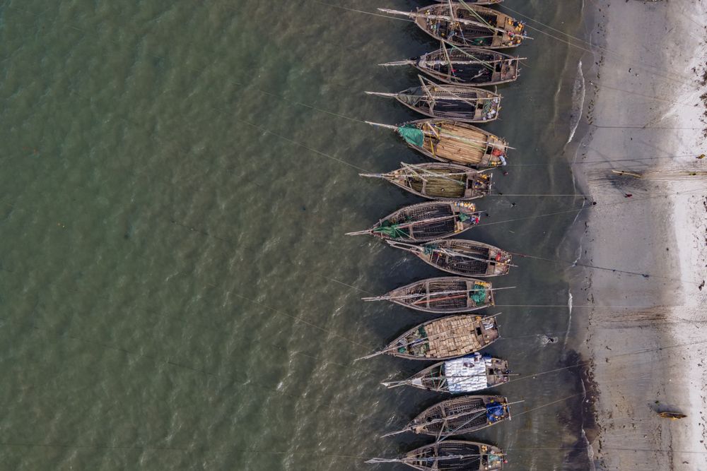 Fishing boats line the shoreline in Tanzania on a quiet afternoon, viewed from above as they rest in the shallow coastal waters.