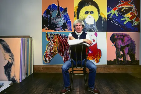 Pop artist Andy Warhol sits in front of artworks at his studio, the Factory, in New York City in 1983.