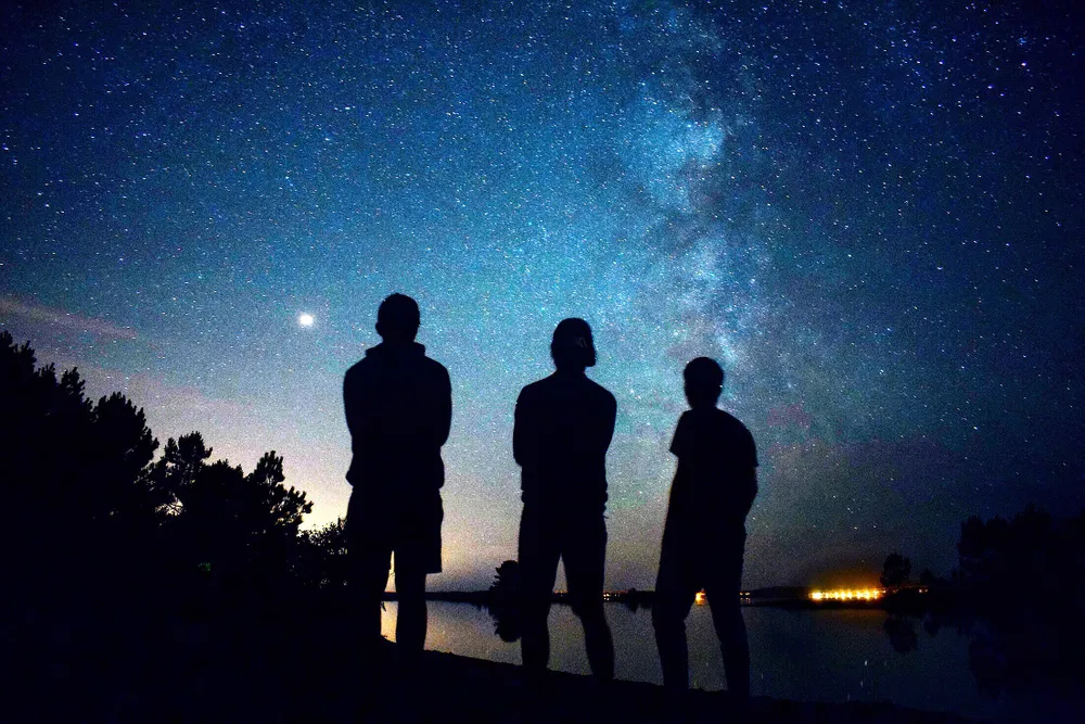 three silhouettes of people stand in front of the starry night sky with the Milky Way visible
