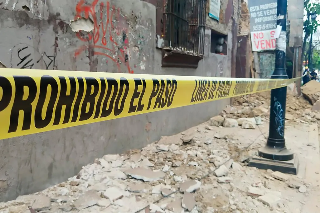 Debris covers a street in Oaxaca. Caution tape reads "Prohibido el paso - linea de policia"