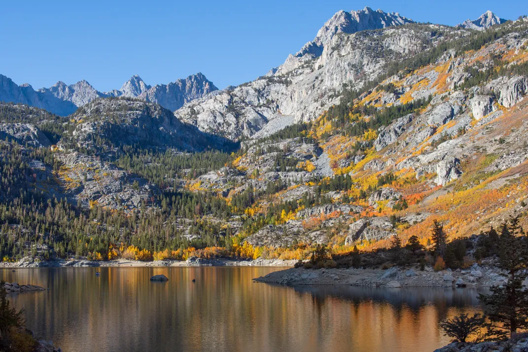 2 - Dozens of trees with leaves of orange, yellow and green dot a lakeside mountain range.