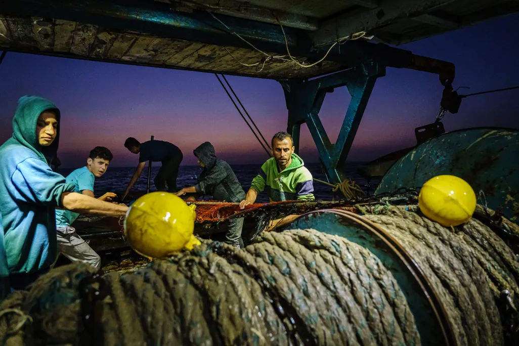 Fishers pull rope by hand at dusk on a fishing vessel in Gaza