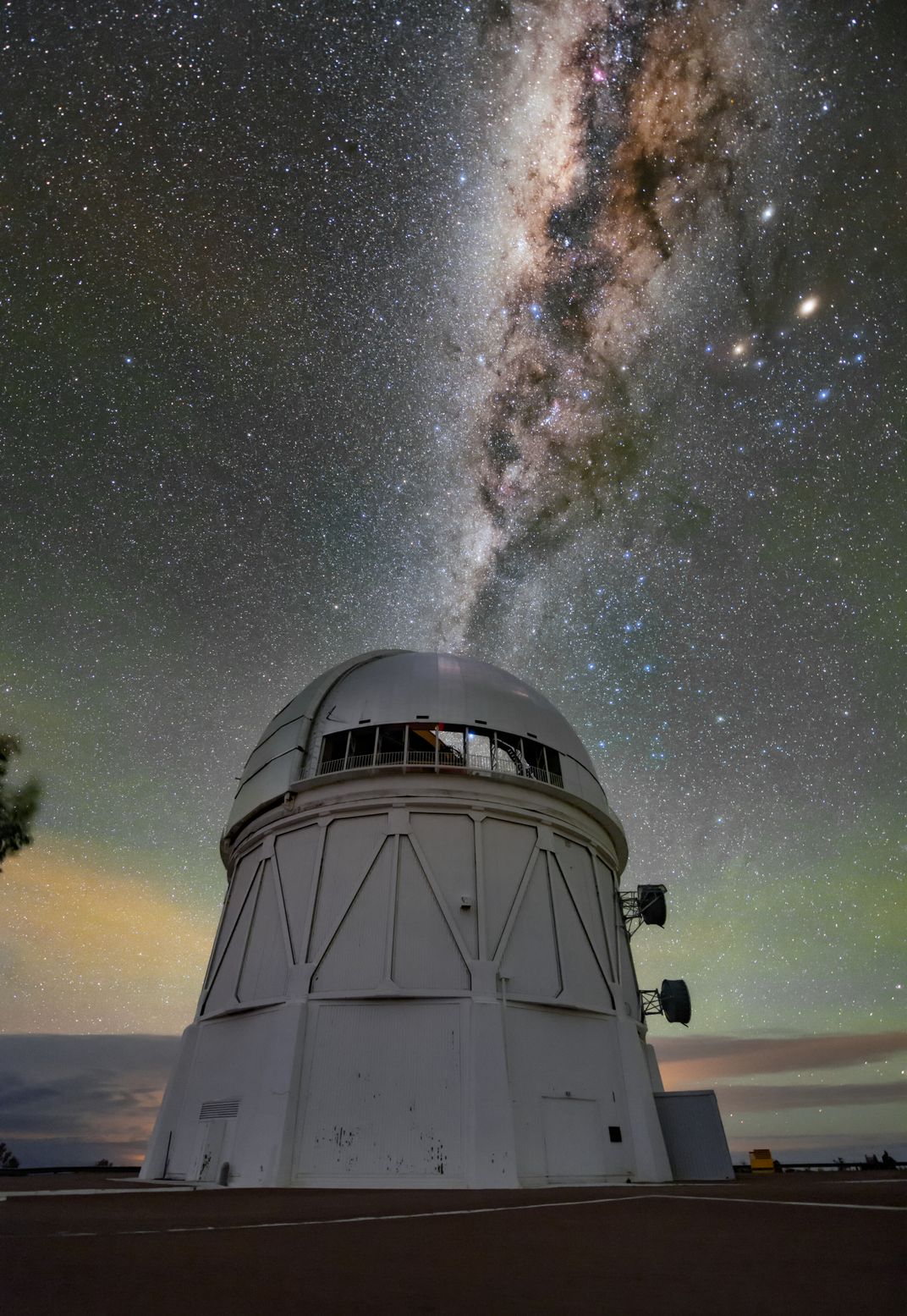 A photograph of the Victor M. Blanco Telescope in Chile with the glow of stars in the sky behind it.