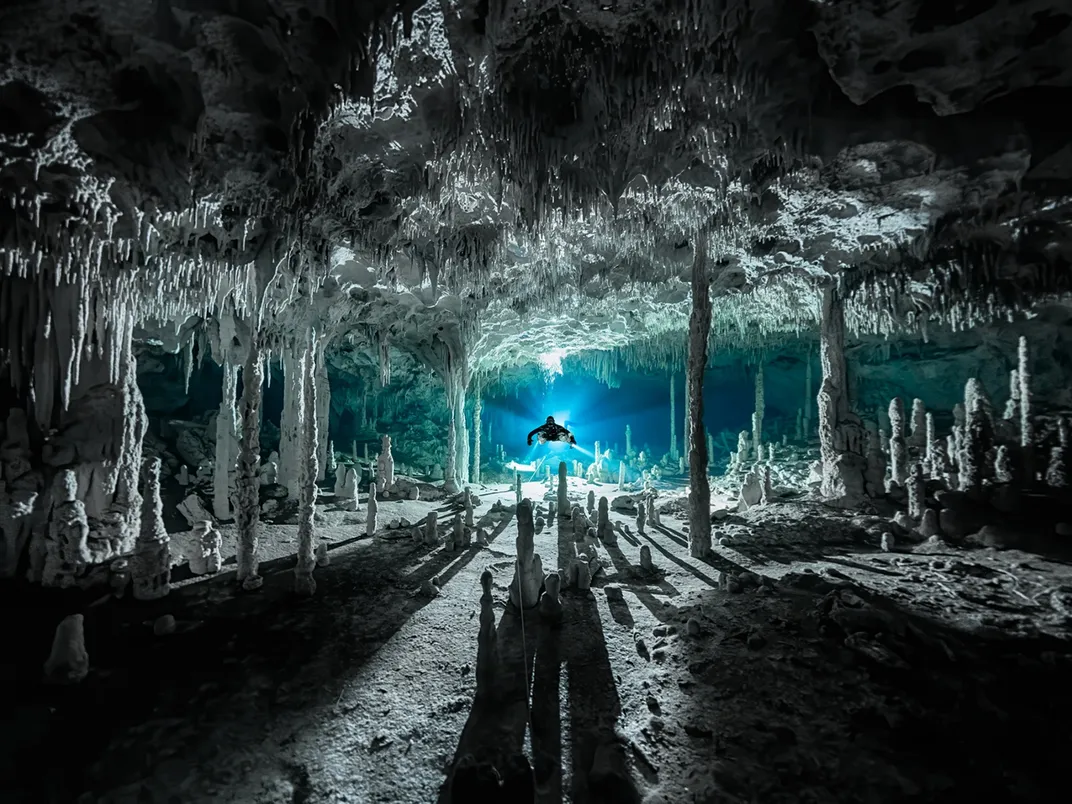 A dark undersea cave with stalagmites and a diver with a light