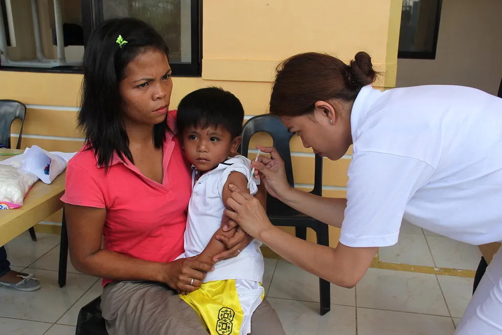 A woman in the Philippines sits with her four year old son as he receives a measles vaccine from a nurse in the aftermath of Typhoon Haiyan in 2013.