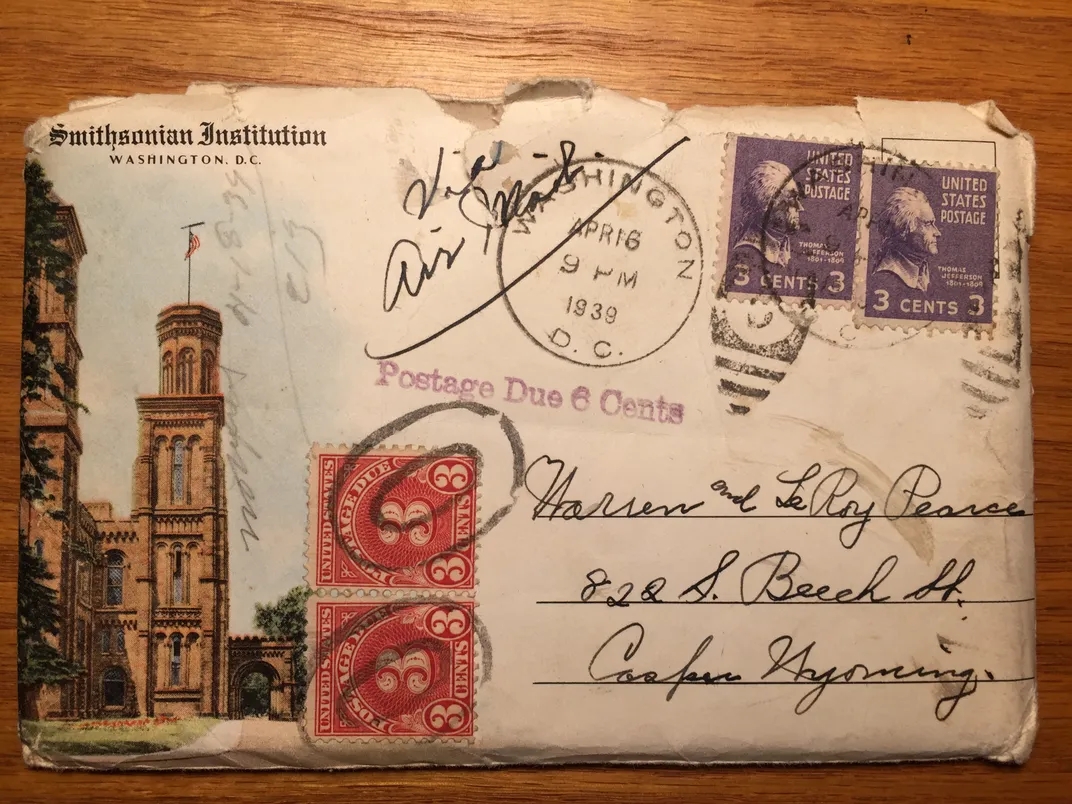 Cancelled envelope featuring the Smithsonian Castle on the left and a stamp on the right dated April, 1939 set on a wood table. 